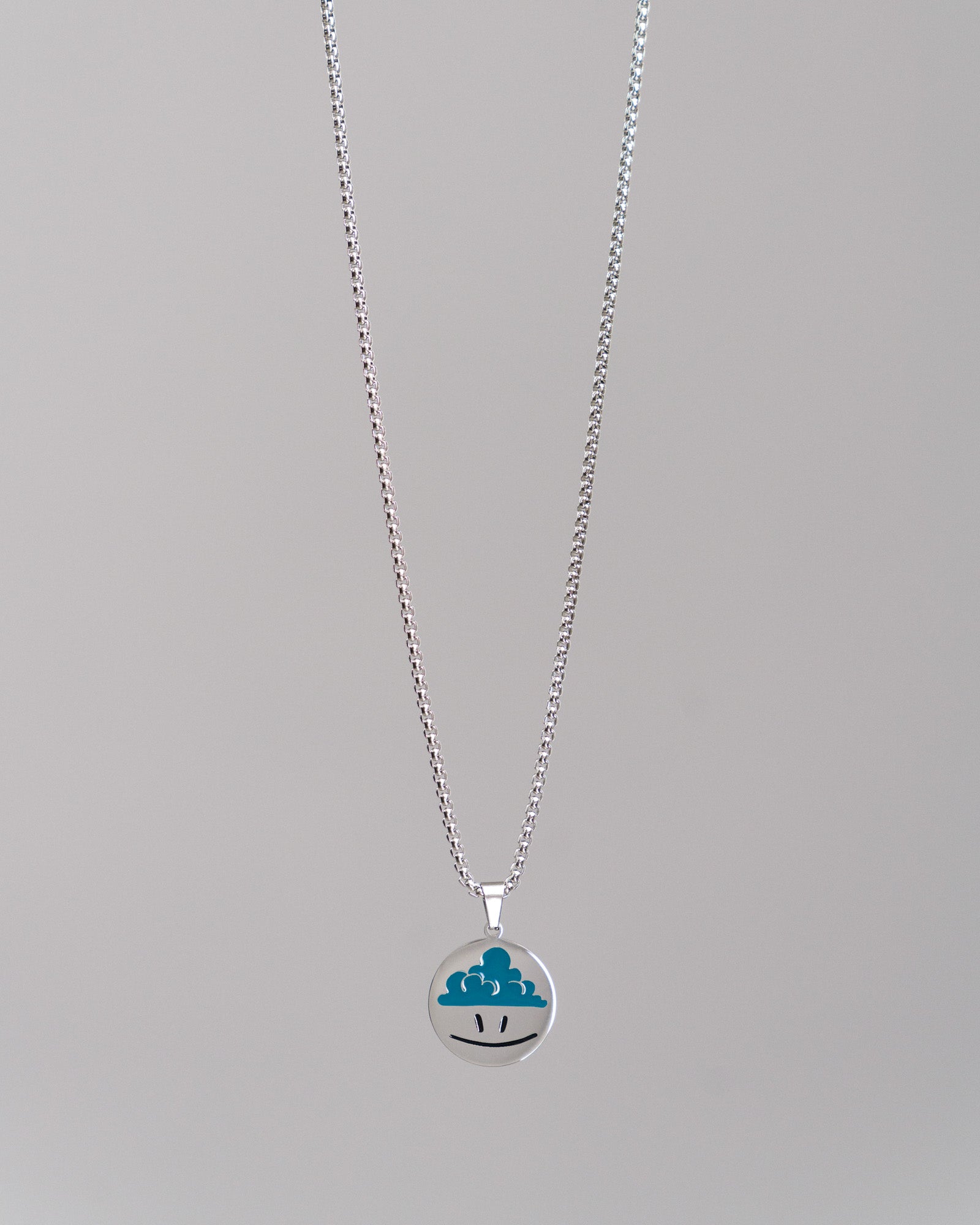 Silberne Gliederkette mit rundem Anhänger; der Anhänger zeigt ein grafisches Wolkensymbol mit zwei schwarzen Augen auf glatter Oberfläche.