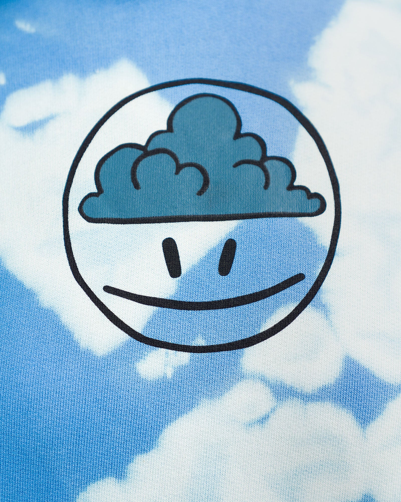 Großaufnahme des zentralen Brustmotivs: eine schwarze Liniengrafik eines Gesichts mit Wolke auf der Stirn, eingebettet in einen Kreis auf blau-weiß gebatiktem Stoff.