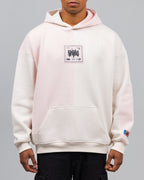 Locker geschnittener Hoodie mit zweifarbiger Vorderseite in Cremeweiß und Rosé. Auf der Brust ein quadratischer Aufnäher mit grafischem Schriftzug „SPARK“ und kleinen Symbolen. Kängurutasche im unteren Bereich.