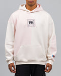 Locker geschnittener Hoodie mit zweifarbiger Vorderseite in Cremeweiß und Rosé. Auf der Brust ein quadratischer Aufnäher mit grafischem Schriftzug „SPARK“ und kleinen Symbolen. Kängurutasche im unteren Bereich.