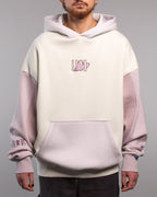 Cremefarbener Hoodie mit fliederfarbenen Ärmeln, getragen von vorn gezeigt. Auf der Brust ist ein rosa Herzmotiv zu sehen, das von fünf senkrechten Linien in dunklem Lila umgeben ist. Die Ärmel sind im Farbblockstil gehalten, die Kapuze ist ebenfalls fliederfarben.