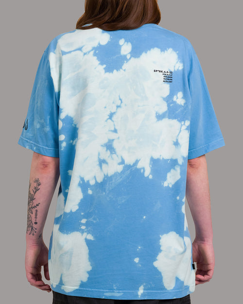 Rückansicht eines blau-weißen Batikshirts mit wolkenartigem Muster. Auf dem oberen Rücken befindet sich ein schwarzer Textprint in versetzter Zeilenstruktur. Das Muster zieht sich unregelmäßig über die gesamte Fläche.