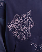 Nahaufnahme des liniengrafischen Brustmotivs. Die Illustration zeigt eine organische, strukturierte Fläche, die an ein abstraktes Tiergesicht oder ein topografisches Relief erinnert. Die feinen Linien sind in Rosa auf dunkelblauem Stoff gedruckt.