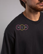 Detailansicht der linken Schulterpartie mit drei stilisierten Smiley-Gesichtern in rosa, gelb und rosa Kreisrahmen – zwei traurig, eines fröhlich in der Mitte.