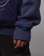 Nahaufnahme des linken Ärmelbündchens. Zu sehen ist ein kleines blaues Weblabel mit hellblauem Sternchenmuster, das an der Naht hervorschaut.