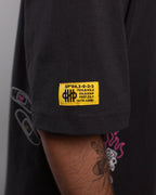 Nahaufnahme des gelben Labelpatches auf dem rechten Ärmel. Die Aufschrift enthält technische Codes und das Logo „SP*RK“. Darunter sind Pflastergrafiken und ein Flammenmotiv zu erkennen.