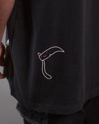 Detailaufnahme der unteren Rückseite mit weißem Linienmotiv einer stilisierten Sense mit lachendem Gesicht. Die Illustration befindet sich über der schwarzen Jeans mit weißer Naht.
