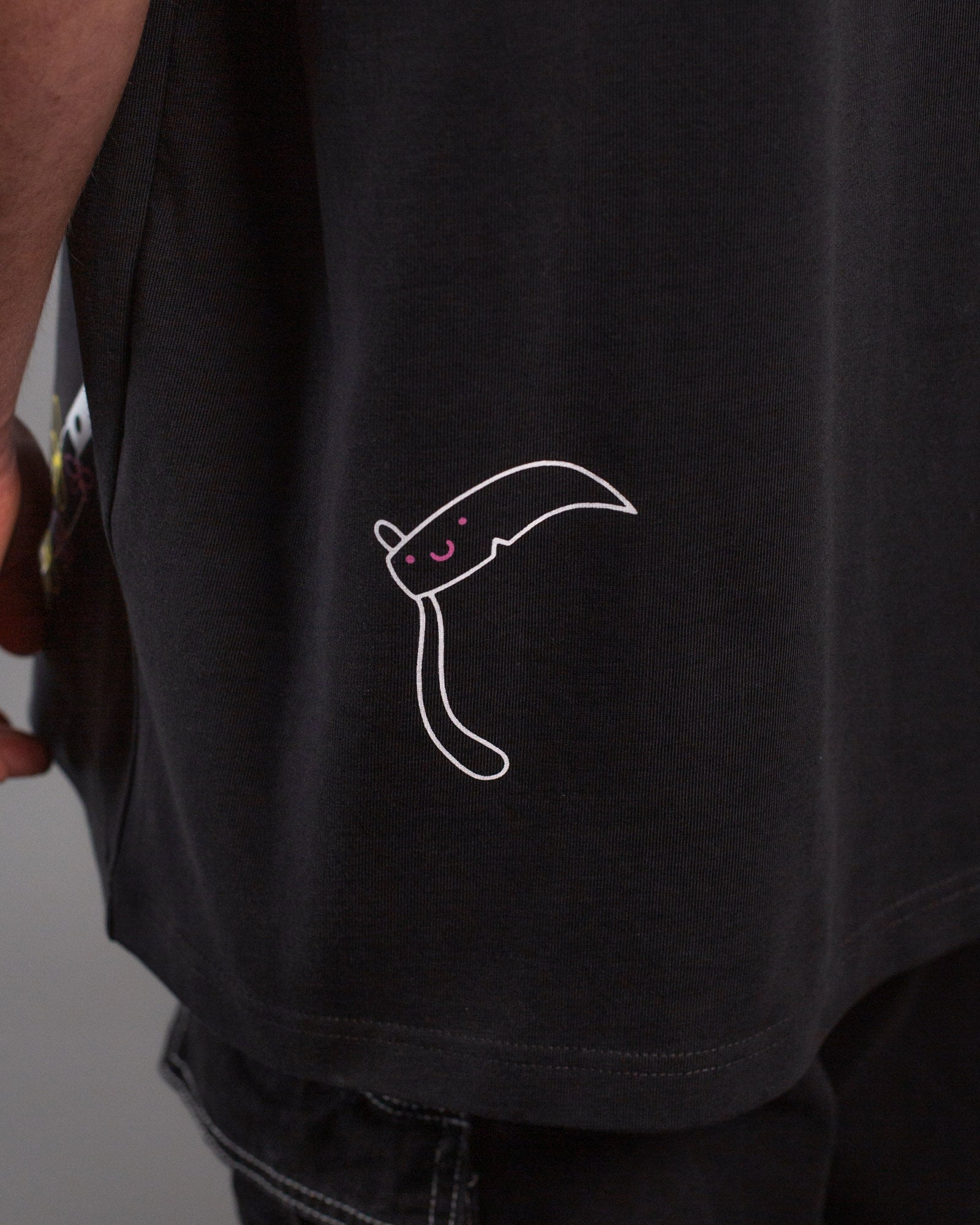 Detailaufnahme der unteren Rückseite mit weißem Linienmotiv einer stilisierten Sense mit lachendem Gesicht. Die Illustration befindet sich über der schwarzen Jeans mit weißer Naht.
