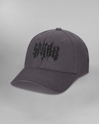 Dunkelgraue Baseballcap in Frontalansicht, leicht von links fotografiert. Auf der Vorderseite ist das Wort „SP*RK“ in schwarzer, fragmentierter Typografie großflächig aufgestickt. Die leicht gebogene Krempe ist tonal abgestimmt und mehrfach abgesteppt.