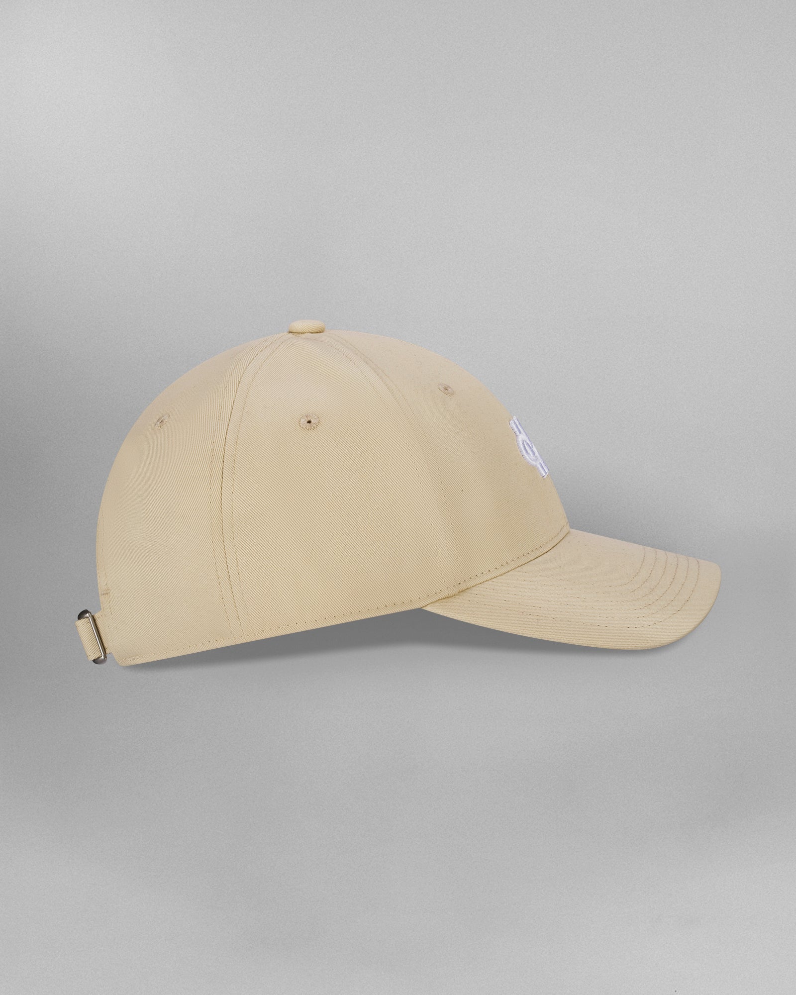 Rückansicht einer beigefarbenen Cap mit verstellbarem Riemen. Auf dem beigen Stoffband ist der weiße Schriftzug „SP*RK“ aufgedruckt. Der Riemen hat eine silberfarbene Metallschnalle, links ist ein blauer Stoffeinsatz sichtbar.