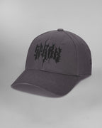 Dunkelgraue Baseballcap in Frontalansicht, leicht von links fotografiert. Auf der Vorderseite ist das Wort „SP*RK“ in schwarzer, fragmentierter Typografie großflächig aufgestickt. Die leicht gebogene Krempe ist tonal abgestimmt und mehrfach abgesteppt.