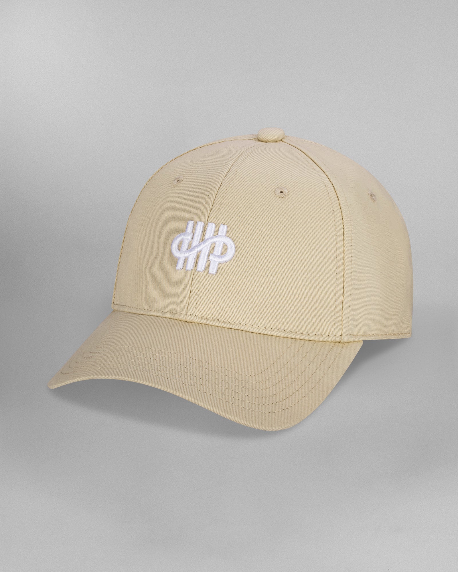 Beigefarbene Baseballcap in schräger Frontansicht, mit geschwungenem weißem Sticklogo aus vertikalen Linien und Schleifenform auf der Vorderseite. Die Kappe zeigt sichtbare Ziernähte und Luftlöcher.