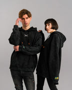 Das Paar steht nebeneinander, beide mit identischem Hoodie. Der Fokus liegt auf dem lockeren, oversized Schnitt und den auffälligen Kordelenden in Orange.