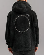  Rückansicht des Hoodies mit großem Rundmotiv aus Stacheldraht-Stickerei auf dem Rücken. Oben rechts auf dem Rücken befinden sich weiße Textdetails mit Code-Zeilen.