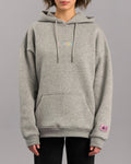 Grauer Kapuzenpullover in lockerer Passform mit Kängurutasche und verstellbarer Kapuze. Auf der Brust ist der Schriftzug „SP/RK“ in bunten Pastellfarben gestickt. Am Ärmelabschluss befindet sich ein kleines rosa Label mit schwarzem Text und grafischen Elementen.