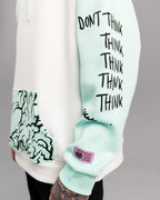 Detailansicht des rechten Ärmels mit schwarzem Textdruck „DON’T THINK THINK THINK THINK THINK THINK“. Darunter befindet sich ein lilafarbenes Labelpatch.