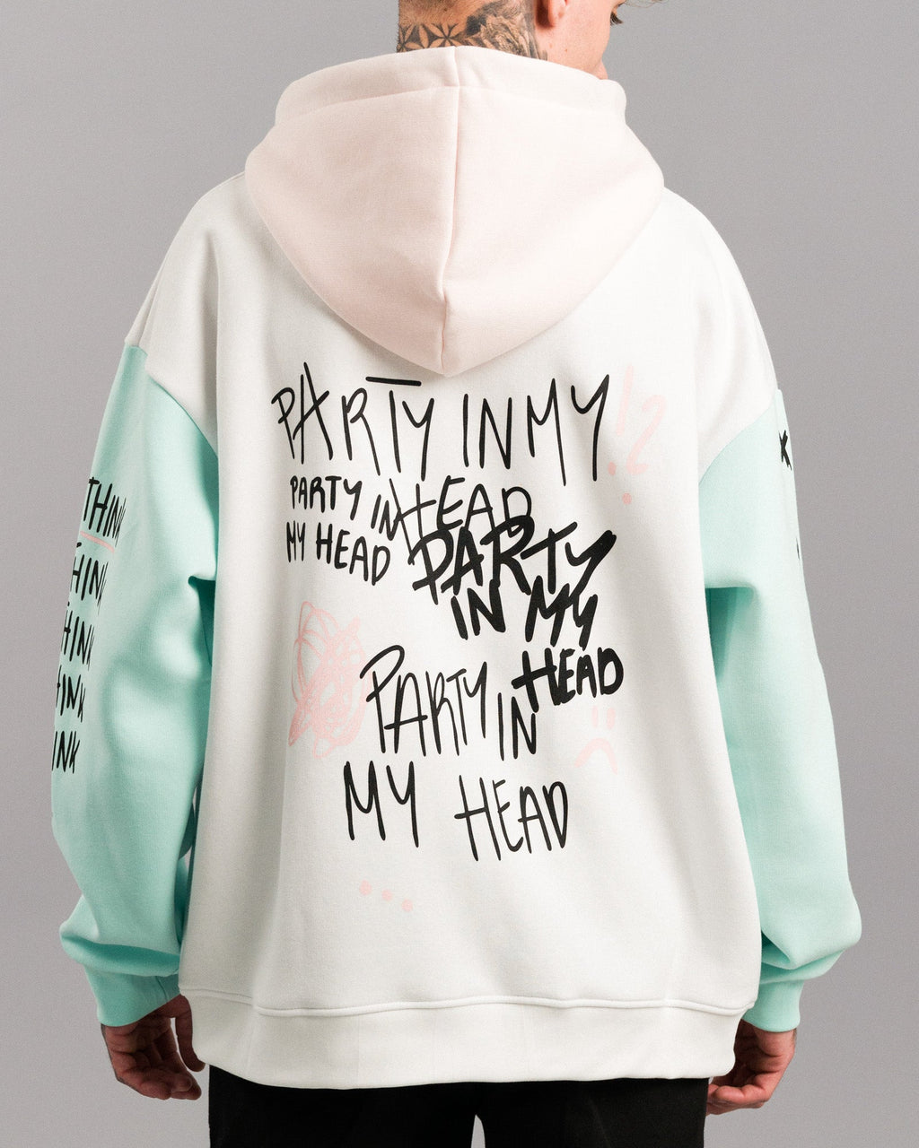 Rückansicht des Hoodies mit mehrfach aufgedrucktem schwarzen Text „PARTY IN MY HEAD“ in verschiedenen Schriftarten. Rosa Kritzelgrafiken wie Planetenring und Fragezeichen ergänzen das Design.