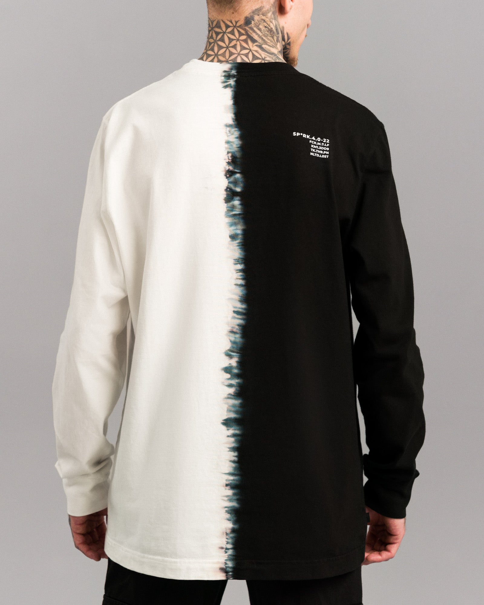 Rückansicht des Shirts mit zentral verlaufender Tie-Dye-Nahtlinie. Linke Rückseite in Weiß, rechte in Schwarz. Oben rechts ist ein weißer Textaufdruck mit technischer Typografie angebracht.
