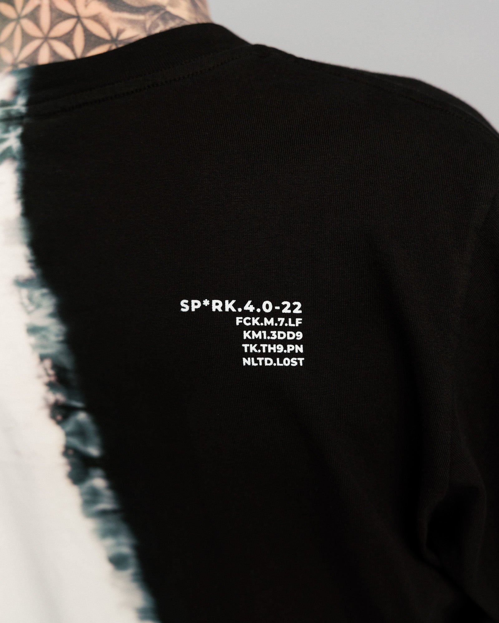 Nahaufnahme der Rückenpartie mit weißem Textdruck auf schwarzem Hintergrund. Aufschrift: „SP*RK.4.0-22“ gefolgt von mehreren kryptischen Codes in Großbuchstaben.