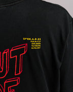 Detailaufnahme des gelben Textfelds auf dem Rücken des T-Shirts über dem „OUT OF IDEAS“-Print, mit kryptischen Codezeilen wie „SP*RK.4.0-22“ und „NLTD.LOST“.