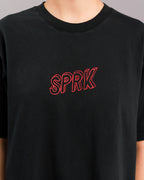 Nahaufnahme der Brustpartie eines schwarzen T-Shirts mit rotem, gesticktem „SPRK“-Schriftzug in Großbuchstaben auf der Vorderseite.