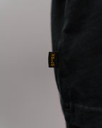Detailansicht des kleinen schwarzen Seitenlabels am Saum des T-Shirts mit gelber „SP*RK“-Stickerei.
