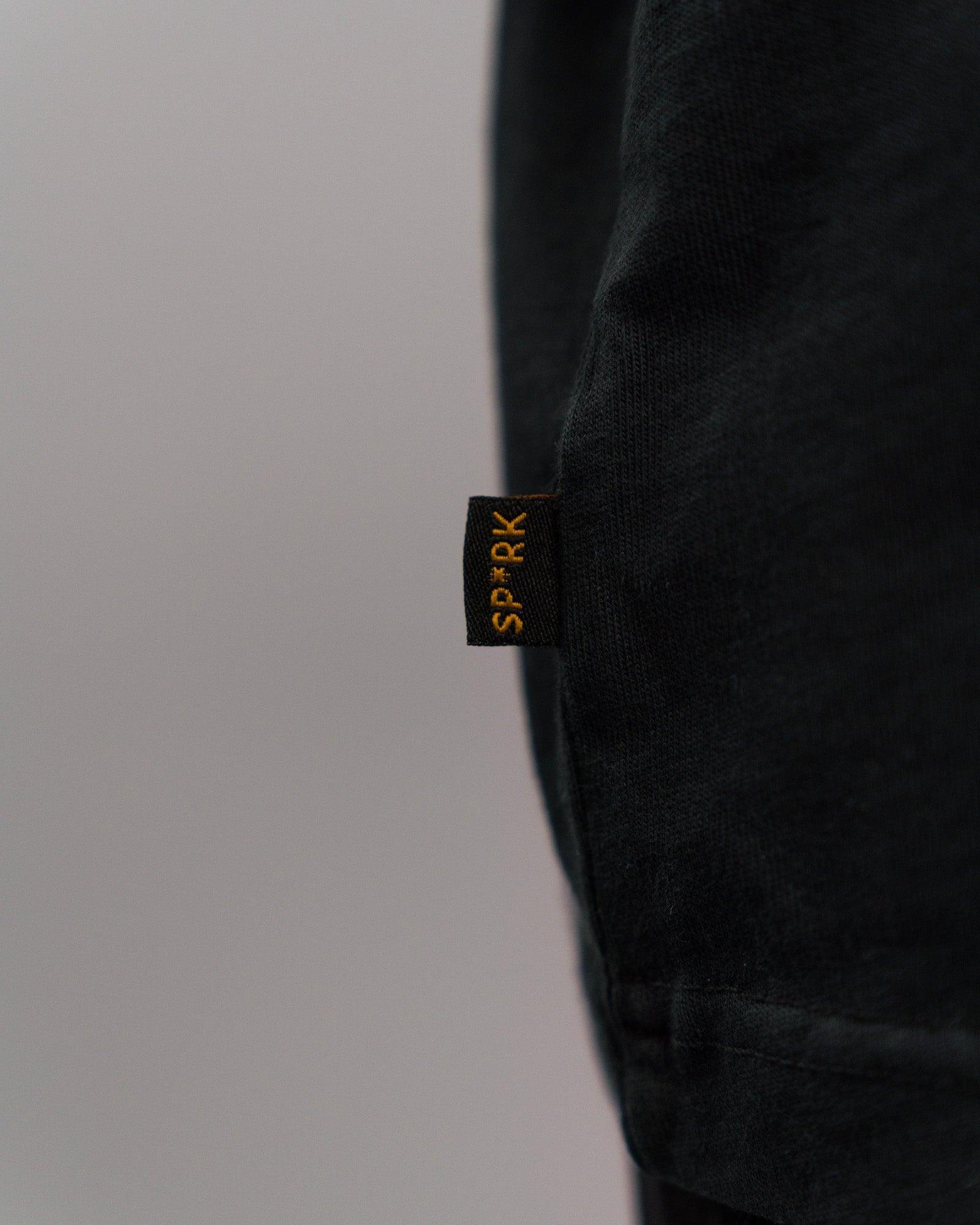 Detailansicht des kleinen schwarzen Seitenlabels am Saum des T-Shirts mit gelber „SP*RK“-Stickerei.