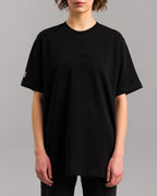 Schwarzes Oversized-T-Shirt mit schwarzer SP/RK-Stickerei auf der Brust, getragen von einer Person in Frontalansicht.