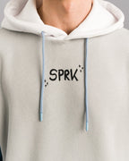 Nahaufnahme des oberen Hoodie-Bereichs. Zu sehen ist der schwarze Schriftzug „SPRK“ auf der Brust sowie der weiße Kapuzenbereich mit hellblauen Kordeln.