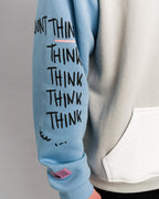 Detailansicht des rechten Ärmels. Der hellblaue Stoff zeigt den mehrfach wiederholten Schriftzug „THINK“ in schwarzer Handschriftoptik sowie ein rosafarbenes Label am Bündchen.