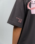 Nahaufnahme des linken T-Shirt-Ärmels mit kleinem rosa Druck: „SP*RK.1.0.–23“, gefolgt von mehreren Zahlen und Buchstabencodes, die technisch oder codiert wirken.