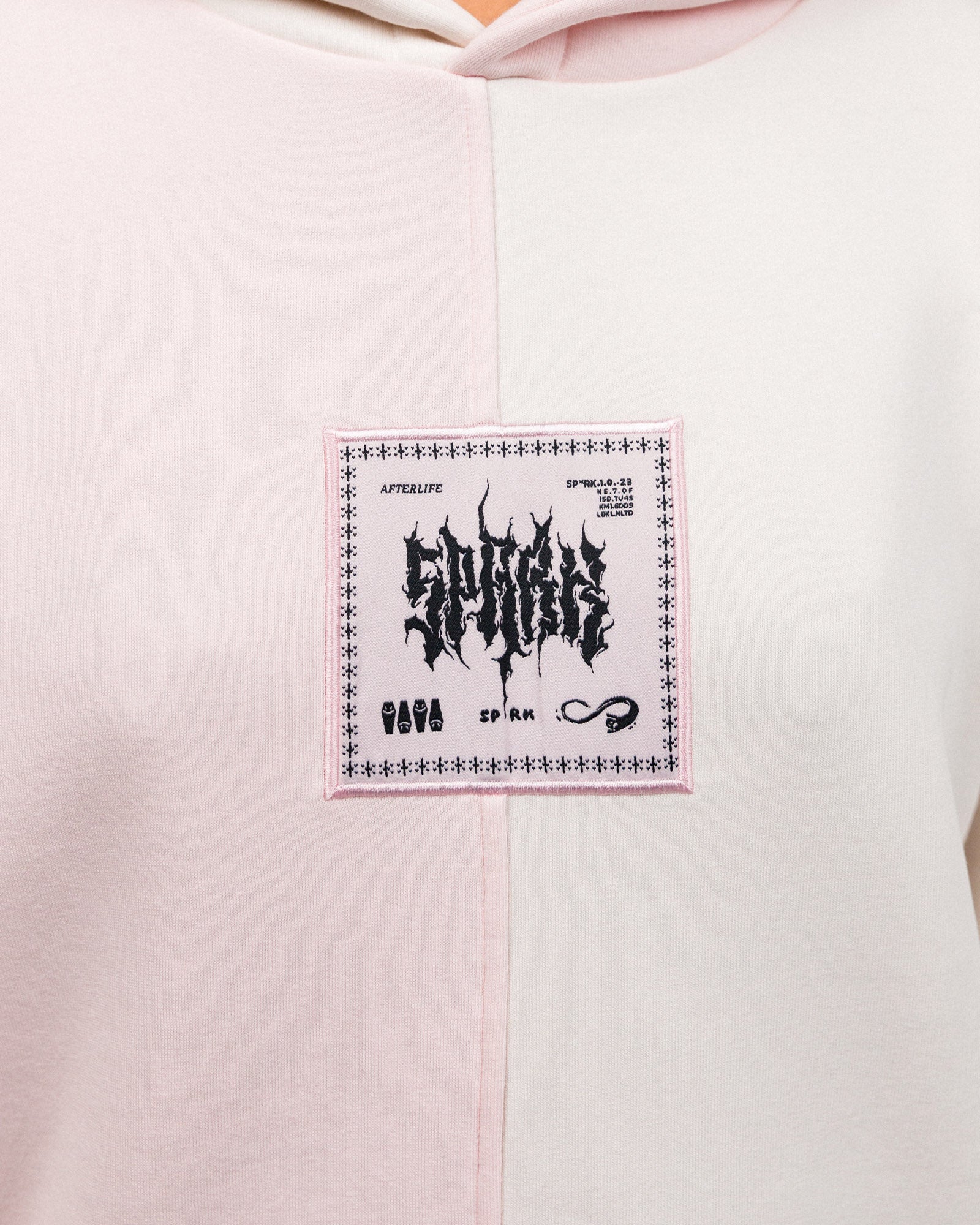 Nahaufnahme des quadratischen Frontpatches in Rosé mit schwarzem Print. Schriftzug „SPARK“ im verzerrten Stil, umgeben von grafischen Elementen wie Särgen, Symbolen und Schriftzügen.