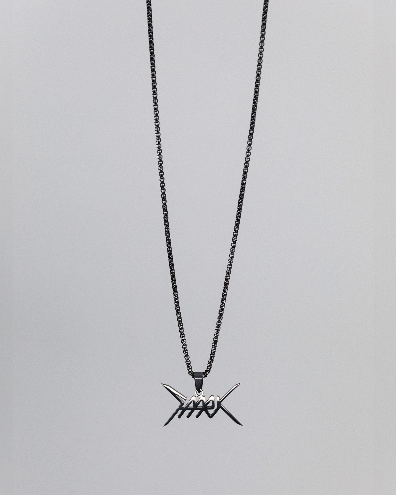 Freigestellte silberfarbene Halskette mit schwarzer Gliederkette und einem markanten, symmetrischen Anhänger in Stacheldraht-Optik, der ein stilisiertes Schriftlogo in Form gekreuzter Spitzen und Linien zeigt.