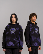 Zwei Personen tragen identische schwarze Hoodies mit lila Punktmuster und zentriertem Frontprint eines stilisierten weißen Gesichts mit Wolkenfrisur in einem Kreis. Beide Hoodies zeigen das Tropfensymbol am rechten Ärmel.