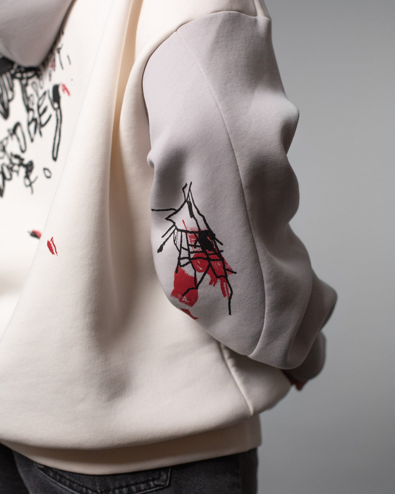 Seitliche Rückenansicht des Hoodies mit Fokus auf den rechten Ärmel. Dort ist eine abstrakte schwarze Liniengrafik mit roten Flächen aufgedruckt, die einem zerbrochenen Objekt ähnelt.