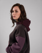 Seitliches Porträt einer Person im Hoodie. Sichtbar sind die kontrastierenden Ärmel in Weinrot, die weinrote Kapuze und die Rückstickerei auf der Schulter.