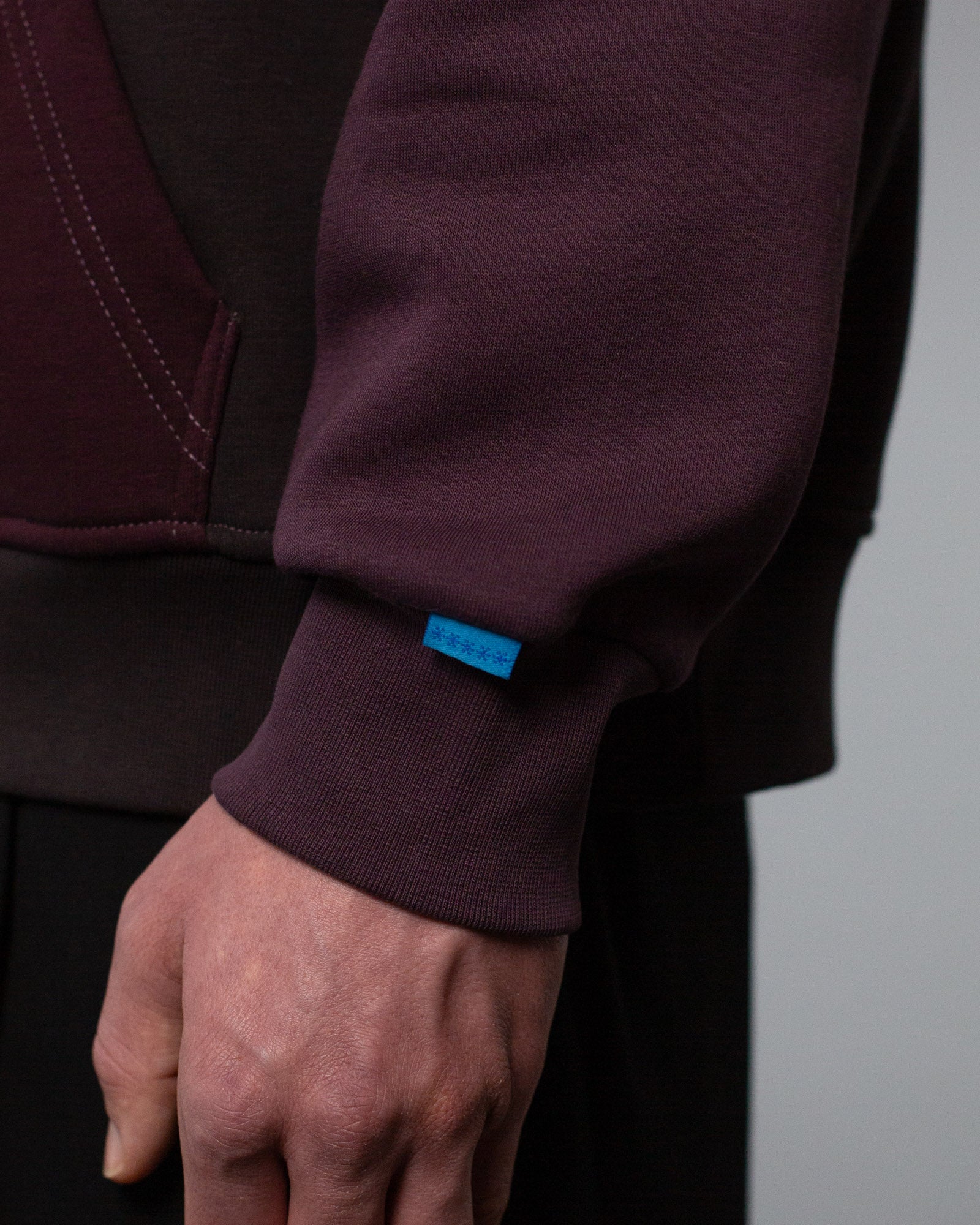Detailansicht des linken Ärmelbündchens mit hellblauem Labelpatch und feiner Naht am Übergang zum Rumpfbereich.