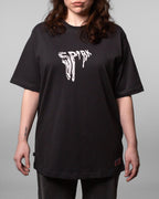 Frontalaufnahme einer Frau im schwarzen T-Shirt mit weißem „SPRK“-Brustprint. Der Schnitt fällt locker und reicht über die Hüfte.
