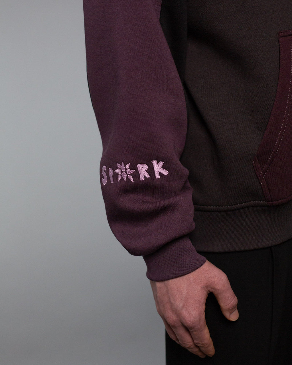 Detailaufnahme des unteren rechten Ärmels mit rosa Stickerei des Wortes „SPARK“, wobei das A durch ein stilisiertes Sternsymbol ersetzt ist.