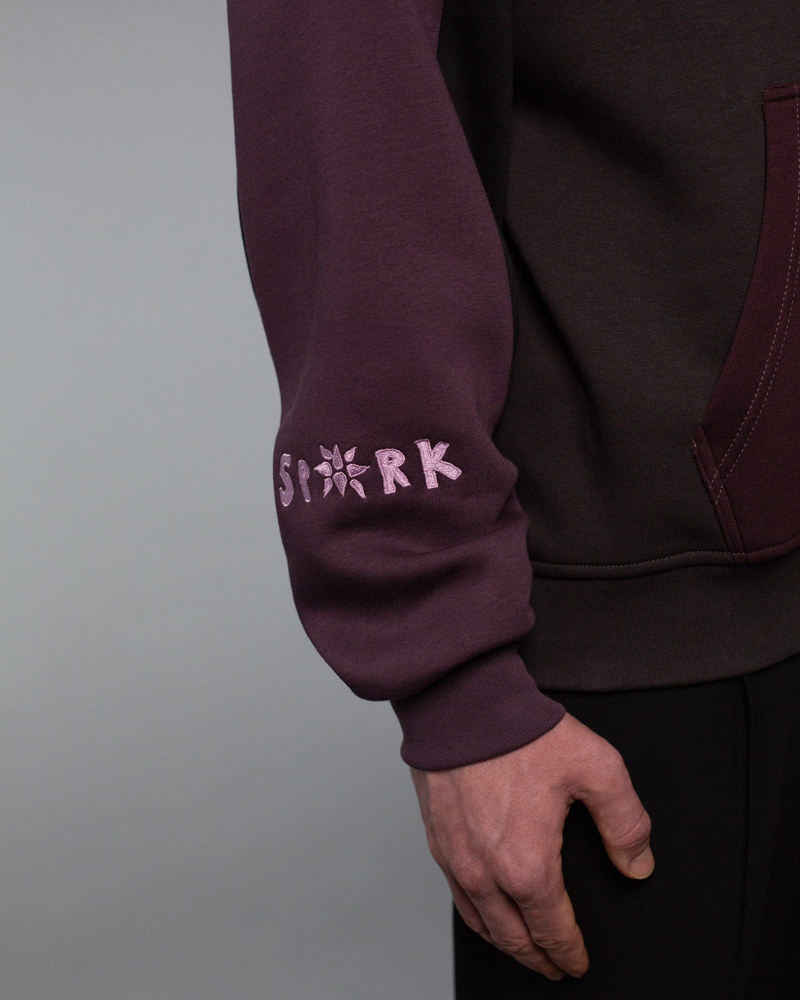Detailaufnahme des unteren rechten Ärmels mit rosa Stickerei des Wortes „SPARK“, wobei das A durch ein stilisiertes Sternsymbol ersetzt ist.