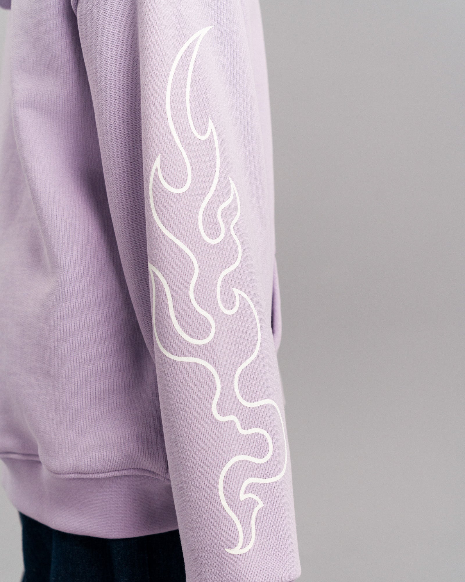 Detailansicht des linken Ärmels des Hoodies mit weißem Flammenmotiv auf fliederfarbenem Stoff. Der Ärmel ist locker geschnitten.