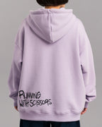 Rückansicht des lilafarbenen Hoodies mit schwarzem, handschriftlich wirkendem Schriftzug „RUNNING WITH SCISSORS“ im unteren Rückenbereich.