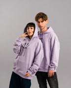 Zwei Personen in identischen lilafarbenen Hoodies mit aufgesetzter Kapuze. Der Smileyprint und das rosa Ärmel-Label sind sichtbar, eine Person hebt die Hand ans Gesicht.