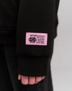 Nahaufnahme eines pinken Ärmel-Labels mit schwarzer Aufschrift, u. a. „SP*RK.3-0-2-2“ und weiteren Codes.