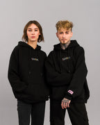 Gleiches Hoodie-Modell an zwei Personen, leicht seitlich stehend mit sichtbarem Logo und Labeldetails.

