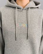 Nahaufnahme des Brustbereichs des grauen Hoodies. Der gestickte Schriftzug „SP/RK“ ist in zarten Farben – Rosa, Mint, Gelb und Blau – aufgebracht. Die Kapuzenkordeln hängen gerade nach unten.