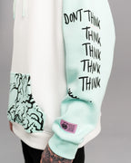 Detailansicht des rechten Ärmels mit schwarzem Textdruck „DON’T THINK THINK THINK THINK THINK THINK“. Darunter befindet sich ein lilafarbenes Labelpatch.