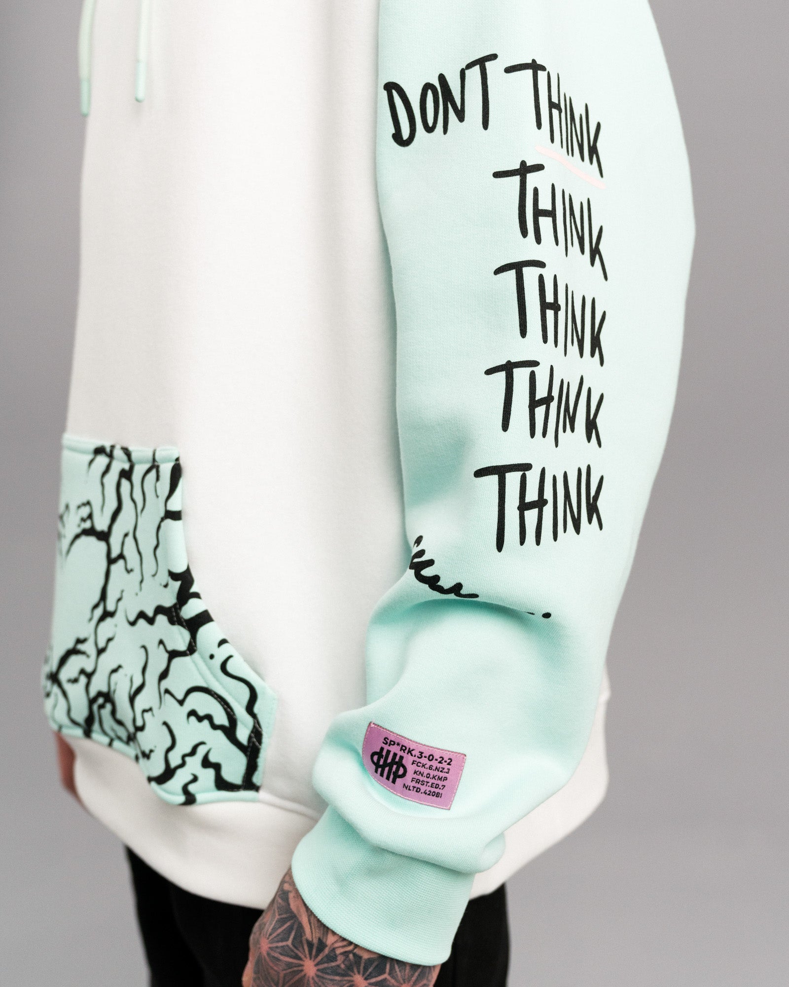 Detailansicht des rechten Ärmels mit schwarzem Textdruck „DON’T THINK THINK THINK THINK THINK THINK“. Darunter befindet sich ein lilafarbenes Labelpatch.