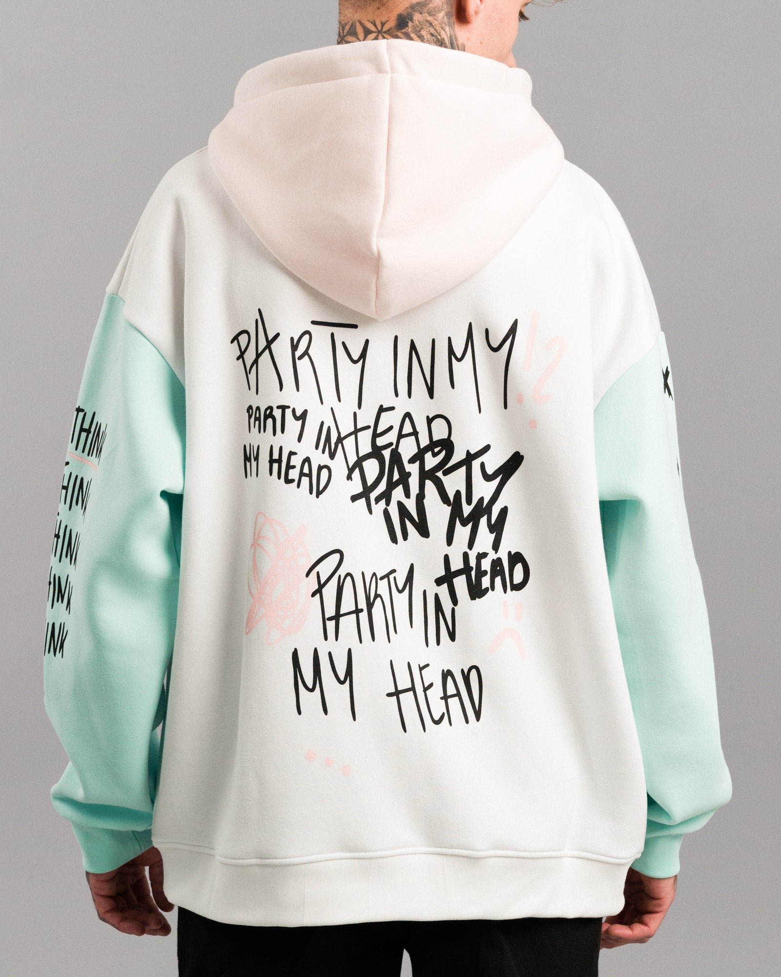 Rückansicht des Hoodies mit mehrfach aufgedrucktem schwarzen Text „PARTY IN MY HEAD“ in verschiedenen Schriftarten. Rosa Kritzelgrafiken wie Planetenring und Fragezeichen ergänzen das Design.