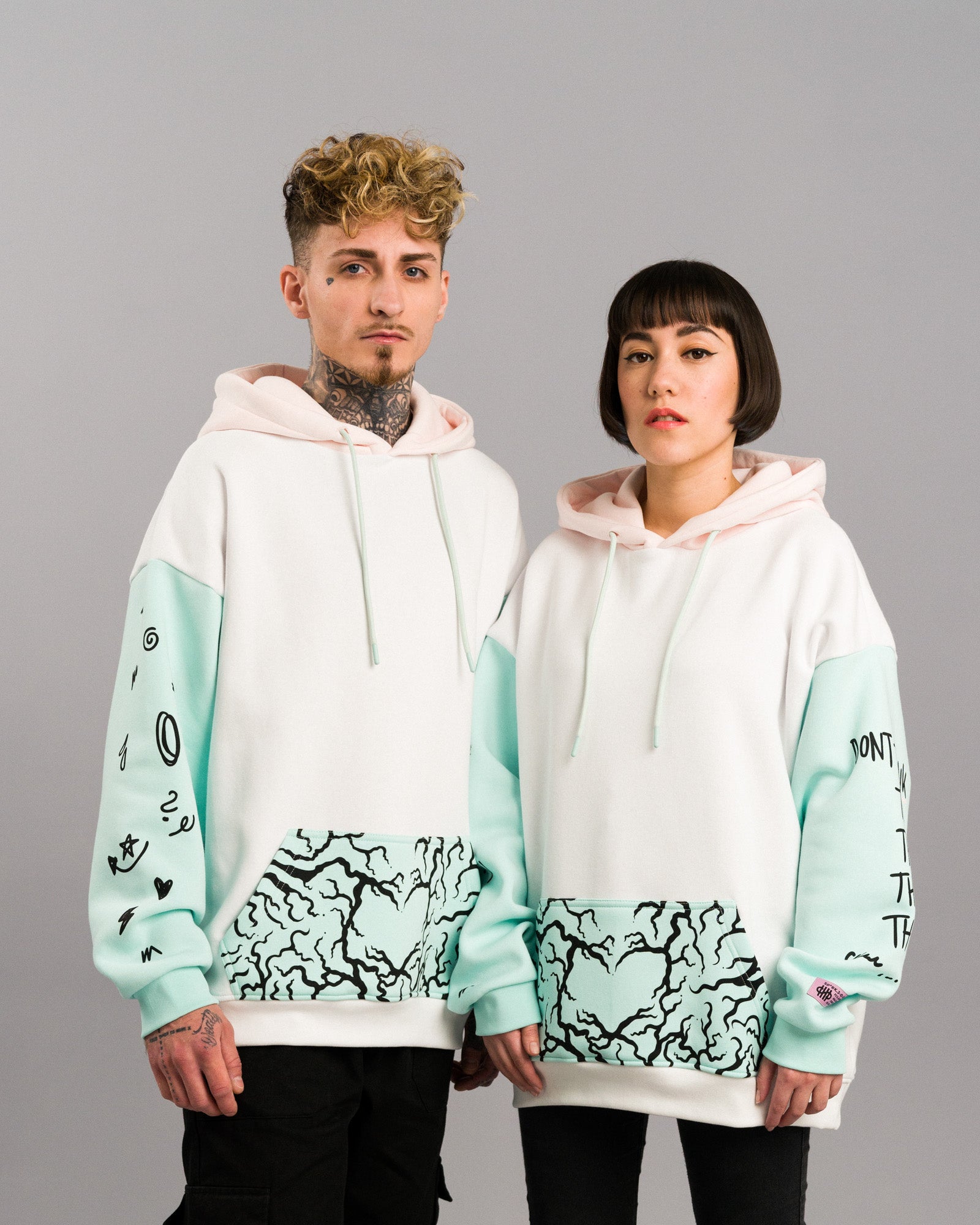 Zwei Personen tragen den Hoodie im Partnerlook. Beide Hoodies zeigen die Vorderseite mit mintfarbener Tasche und hellrosa Kapuze.